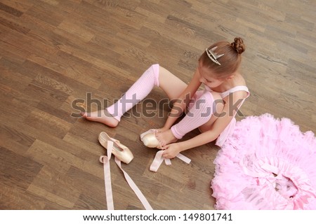 Caucasian little ballerina puts on pointes while sitting on an old wooden floor in the ballet hall
