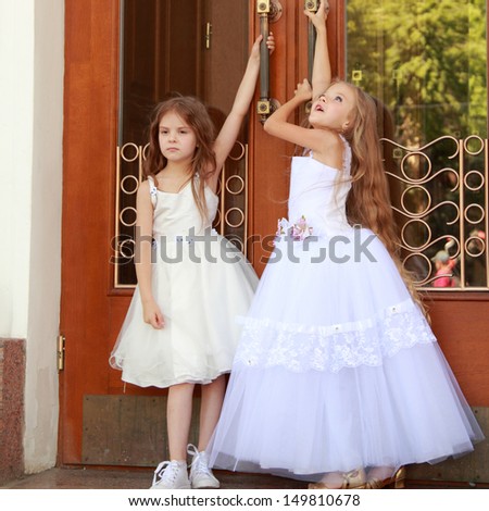 Young girl in white wedding dresses are trying to open the big doors to the building outdoors