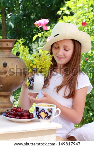 Image of a beautiful young girl in a cute hat is drinking tea from an old antique Russian samovar and the service/Russian antiques and national traditions