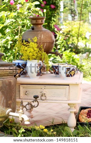 Old rusty samovar tea and ceramic dinner service in the summer garden/Antique Russian samovar