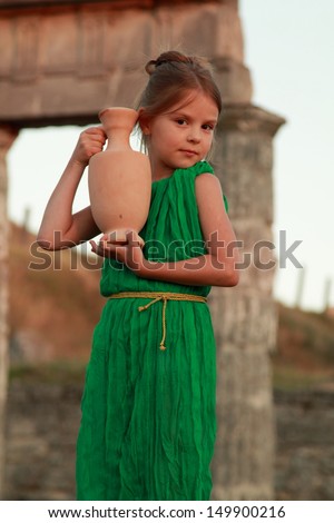 Smiling young girl in a vintage dress from the ancient Greek amphora on the excavation of the ancient city/Little Greek goddess on the ruins of the Greek city