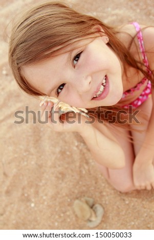 Beautiful cheerful young girl sitting on the sand and holds a large seashell on a summer theme