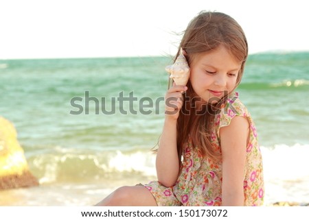 young girl in a summer dress with a seashell sits on the shore of the Black Sea on a hot sunny day