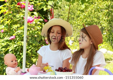 Girls dressed in retro styles in white dresses and a hat are playing and eat cherries in the summer garden