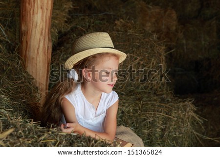 Beautiful little girl in a hat sitting on the hayloft with a book to read and play
