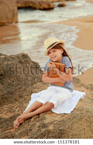 Adorable little girl reading book near the ocean