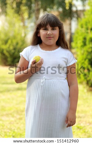 Lovely fat girl with a sweet smile and long brown hair holding a picnic basket and eating an apple in a sunny summer day
