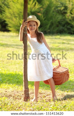 Beautiful young girl with a sweet smile and long, healthy hair is holding a basket for a picnic in a park in sunny summer day