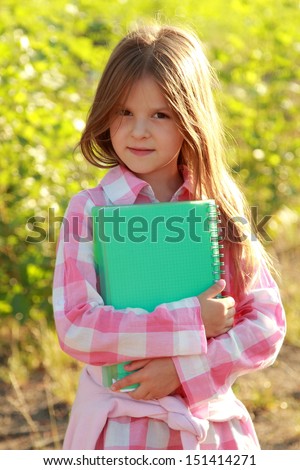 Lovely schoolgirl holding notebook and studying plants in the forest on a school lesson outdoors/Young naturalist