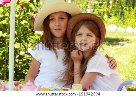 adorable little girls dressed in retro styles in white dresses and a hat are playing and eat cherries in the summer garden outdoors