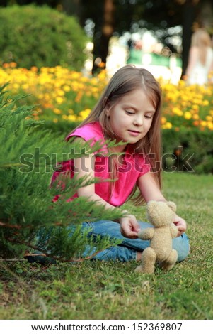 Lovely girl hugging brown teddy bear and sitting down on green grass meadow