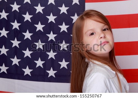 Joyful little girl with long hair and a beautiful smile on the background of the flag of the United States