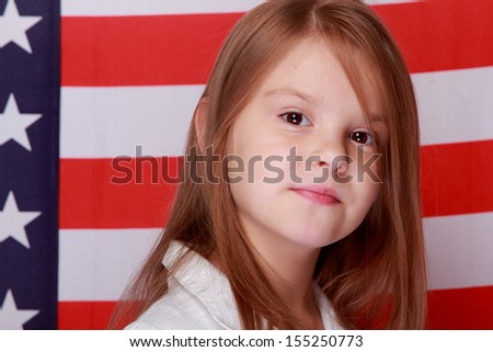 Adorable joyful little girl with long hair and a beautiful smile on the background of the flag of the United States