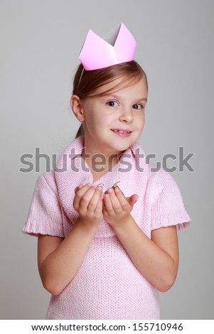Image emotional joyful young girl with a beautiful smile in a knitted dress with a crown holding a gift on a gray background on Holiday/Little girl princess