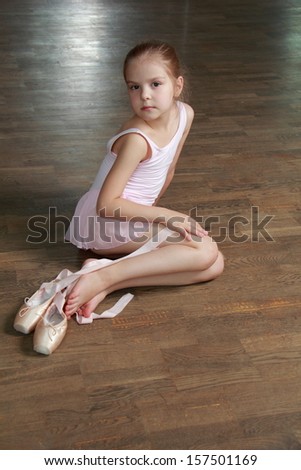 European smiling ballerina sitting on an old wooden floor wearing ballet shoes