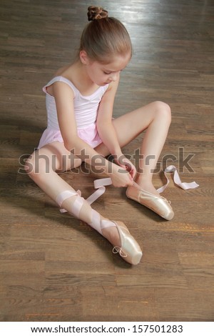 Young ballerina puts on pointe in ballet class at the old wooden dance floor