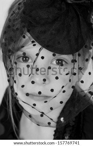 Black and white image of beautiful emotional little girl in a black hat with a veil on Holiday
