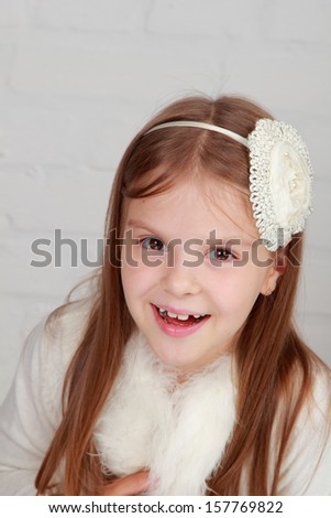 Portrait of a beautiful happy cheerful little girl with a sweet smile in white suit and with hair on light background