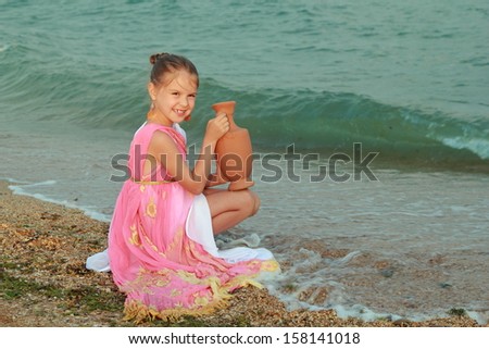 Caucasian sweet young girl in pink tunic in antique style is holding an antique amphora on the sea coast/Greek goddess of beauty