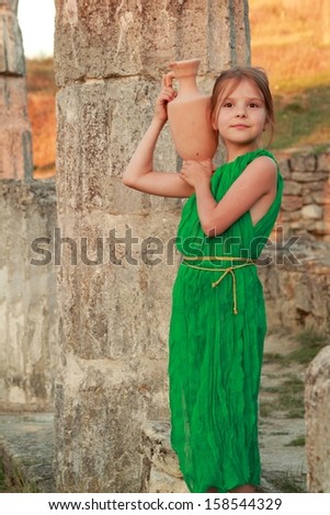 Joyful smiling girl in a beautiful emerald green dress with an amphora in the role of the Greek goddess/Ruins of the ancient city of Pantikapaion in the modern city of Kerch, Crimea, Ukraine