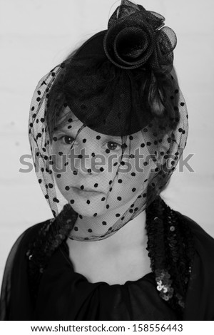 Black and white image of beautiful emotional little girl in a black hat with a veil on Holiday