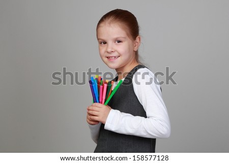 Studio portrait of a beautiful little schoolgirl with a sweet smile holding felt pens on a gray background