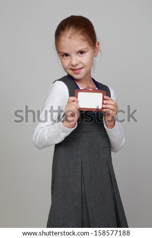 Smiling happy little schoolgirl with a blank name tag on a gray background on Education