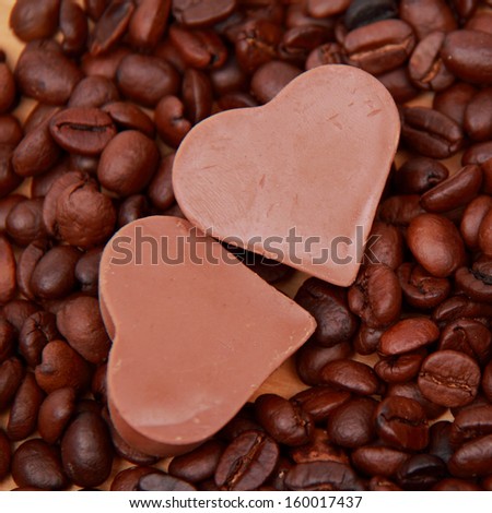 Chocolates in the form of heart with lots of coffee beans over light brown wooden background/delicious chocolate heart symbol candies and dark brown coffee beans