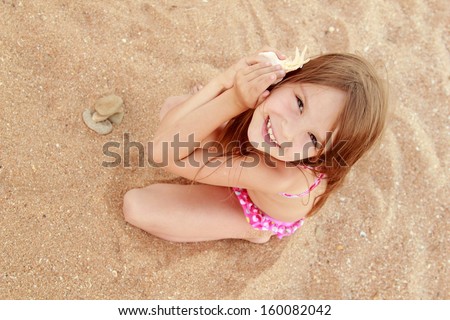 Beautiful cheerful young girl sitting on the sand and holds a large seashell on a summer theme
