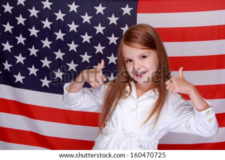 Adorable joyful little girl with long hair and a beautiful smile on the background of the flag of the United States