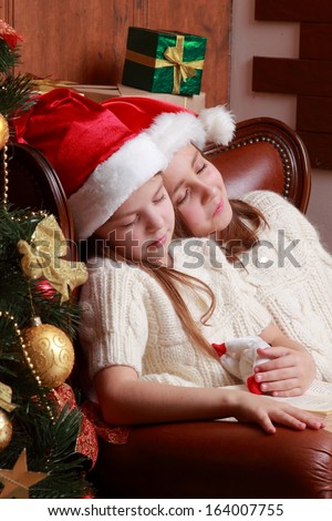 Beautiful european young girls sitting in vintage arm chair pretend sleeping and waiting on Santa\'s presents