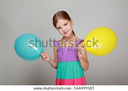cute little girl in a bright sundress holding balloons on gray background on Holiday