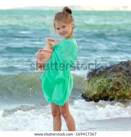 Greek smiling little girl in tunic holds ancient amphora/Cute girl in a beautiful dress is the Greek goddess of the sea and looks into the distance