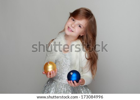 Emotional pretty little girl with a sweet smile holding a yellow and blue christmas balls