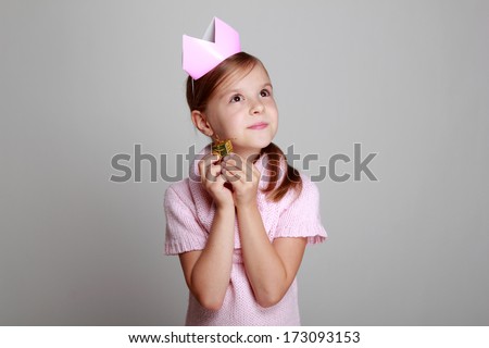 Studio image of a beautiful cheerful little girl in a pink knitted dress with a crown on his head on a gray background on Holiday