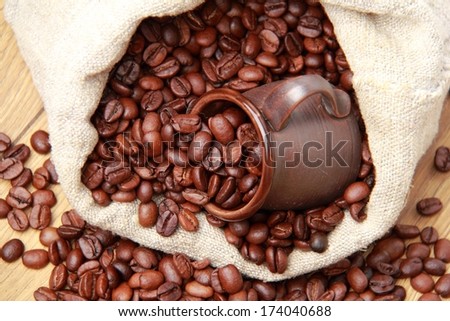 Roasted coffee beans with ceramic dark brown coffee cup over beige burlap  coffee bag
