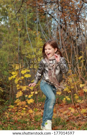 Outdoor image of pretty caucasian kid running in golden autumn forest/Portrait of female european kid playing autumn park