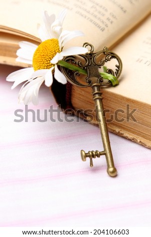 Beautiful vintage key with fresh chamomile and old book isolated on white