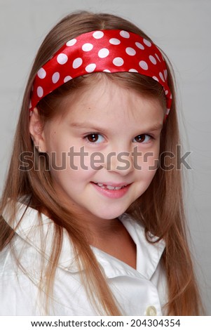 Portrait of lovely cheerful young girl with beautiful hair of red ribbon with polka dots on a gray background
