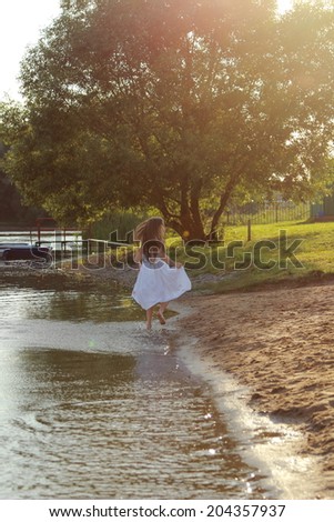 Charming little girl in a white dress on the lake at sunset