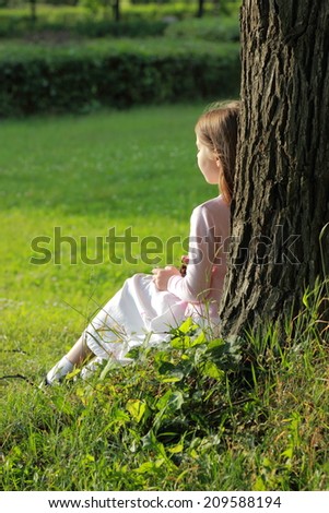 Adorable happy little girl in white dress sitting under a tree and eats cherries on a sunny summer day in the woods