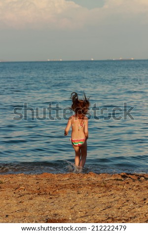 Cute cheerful young girl in a bathing suit running and having fun at the beach near the water theme of travel and holiday