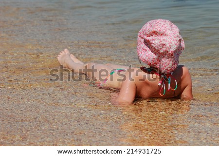 Cute little girl in a swimsuit and a panama hat lies in the water on the shore of the Black Sea in Crimea, Russia
