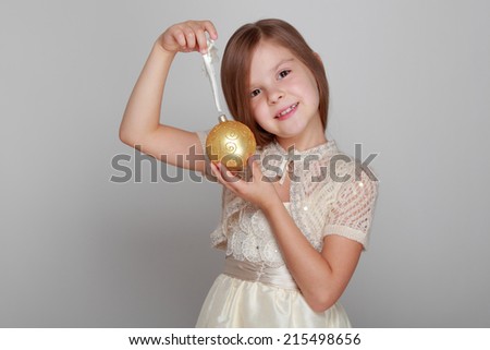 Beautiful emotional little girl holding a Christmas ball on a gray background