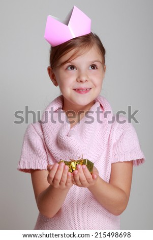 Portrait of charming smiling child in a pink knitted dress with a pink crown on her head holding a small gift on Holiday