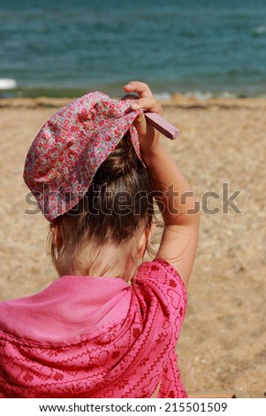 Little girl sitting on the beach with his back to the camera in summer sunny day Kerch, Crimea, Russia