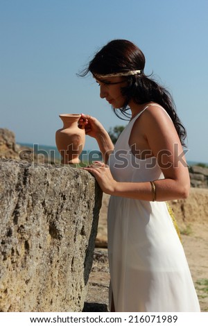 Attractive young girl with long dark hair in a white long tunic in the Greek style walking in the excavations of the ancient city Nymphaeum, village Geroevskoe, Republic of Crimea