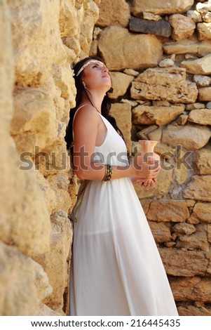 Lovely young woman in a long white dress in Greek style keeps ancient amphora to the ancient site Nymphaeum, village Geroevskoe, Republic of Crimea, Russia