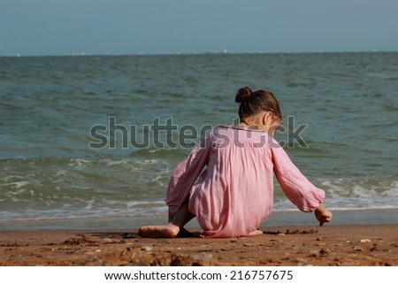 Beautiful little girl wearing light pink dress and playing with pebbles over seaside