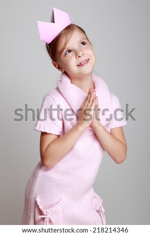 Image of a cute happy little girl with a pink crown posing and smiling at the camera on a gray background on Beauty and Fashion